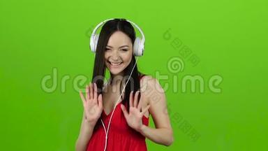 女孩通过耳机听欢<strong>快</strong>而<strong>充</strong>满活力的音乐。 绿色屏幕。 慢动作